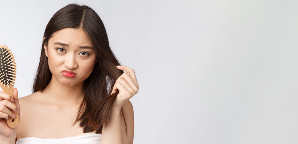 upset stressed young asian woman holding damaged dry hair on hands over white isolated background